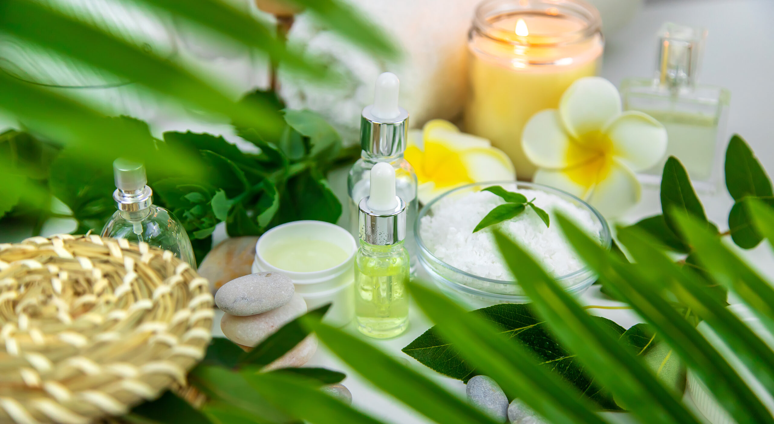 Boccette di profumo circondate da candele profumate, fiori e foglie
